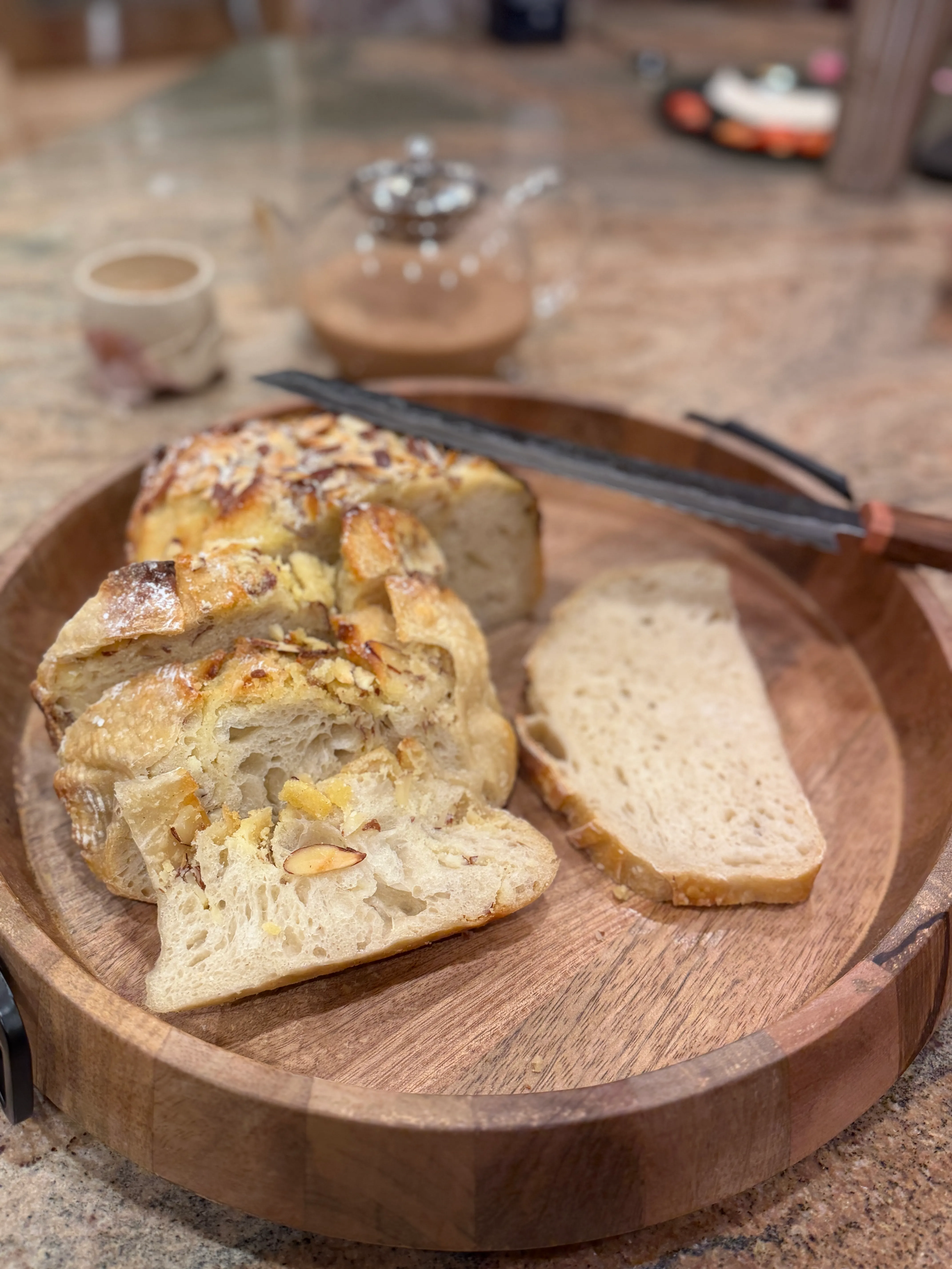 A sliced almond-topped sourdough loaf on a round wooden board